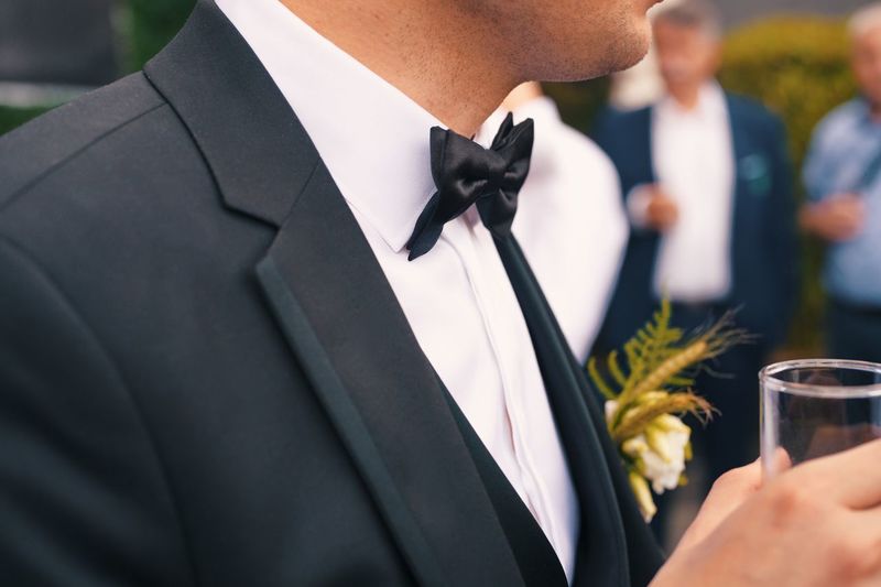 Midsection of groom in formal suit holding glass of drink