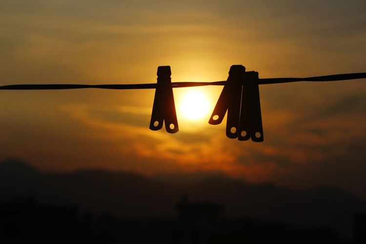 Low angle view of clothespins on rope against sky during sunset