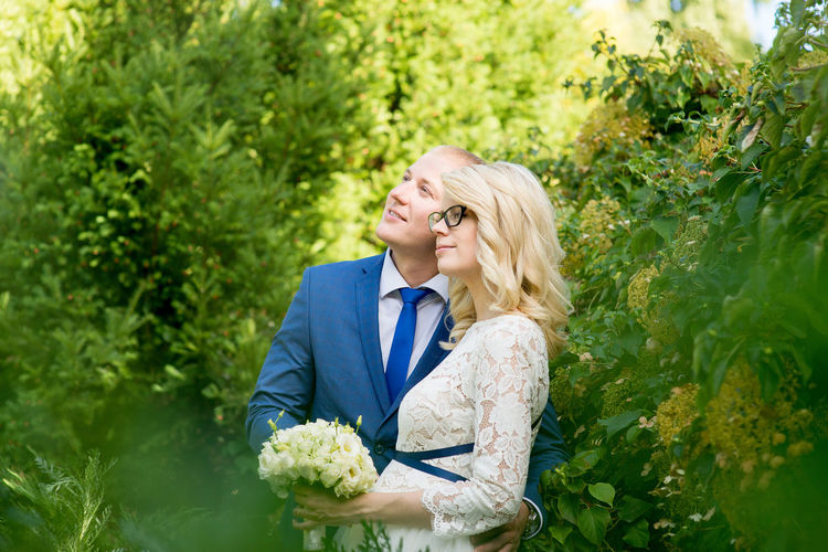Bride and groom embracing while standing amidst plants at park