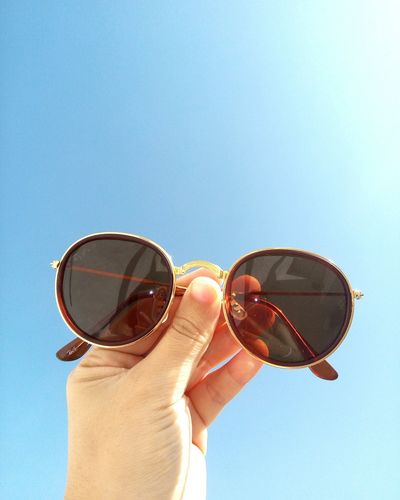 Close-up of hand holding sunglasses against clear sky