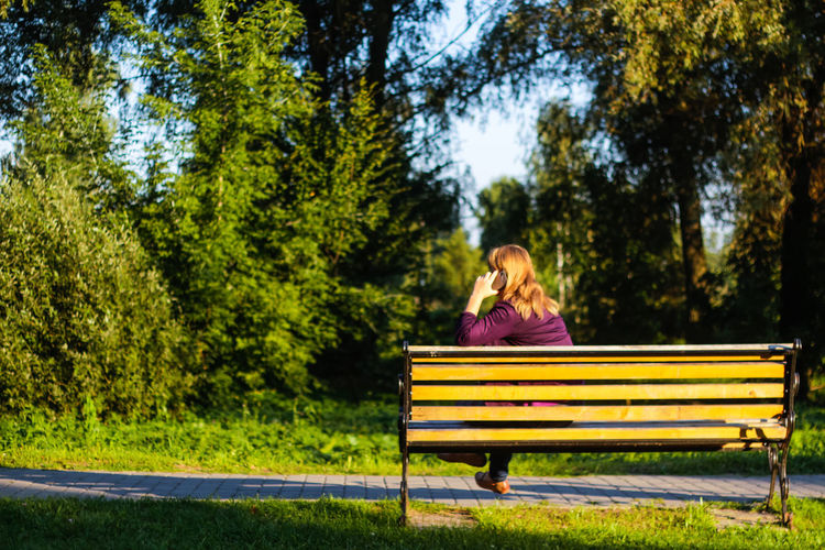 Blond woman talking, speaking on the phone outside, outdoor. 40s years old woman in purple blouse 