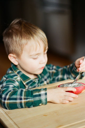 Film photo of a little boy eating a dragon fruit with a spoon.