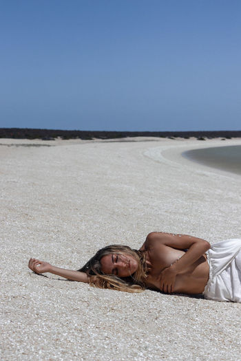 Young blonde woman in white dress lying on the floor due to heat stroke on paradisiacal shell beach