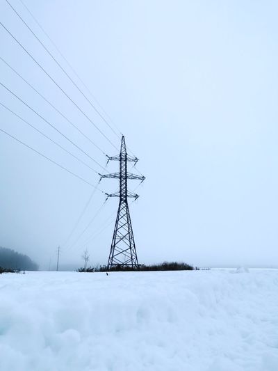 Electricity pylon on snow covered land against sky