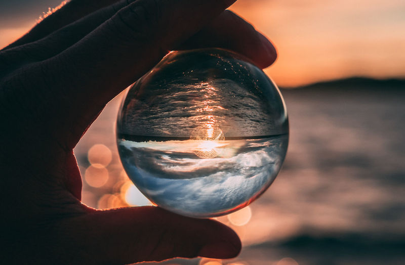 Close-up of hand holding crystal ball at beach during sunset