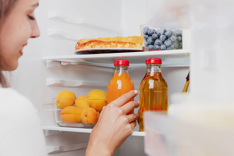 Woman hand taking, grabbing, picking up juice glass bottle out of open refrigerator shelf, fridge