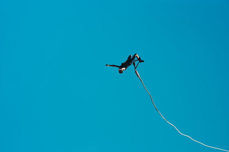Low angle view of man bungee jumping against clear blue sky