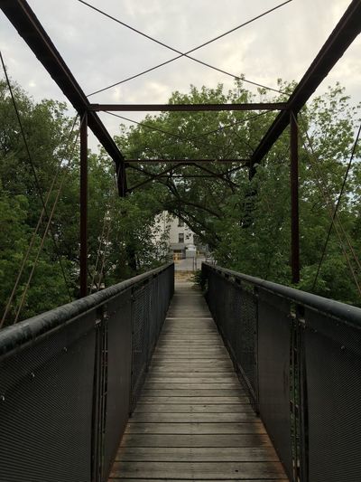 Footbridge amidst trees against sky
