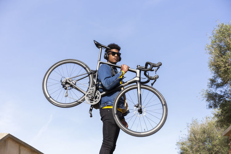 Young man carrying bicycle under clear blue sky