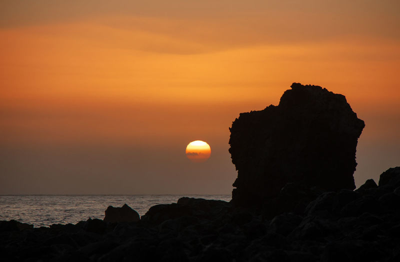 Silhouette rock formation on sea against sky during sunset