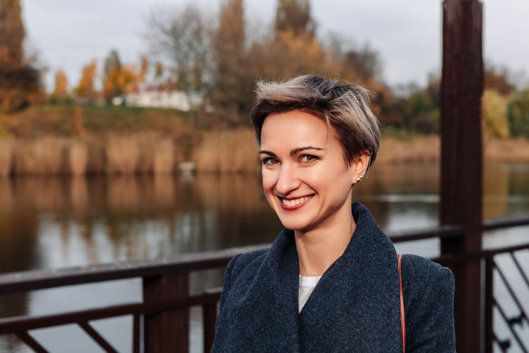 A woman smiles broadly near the river in autumn
