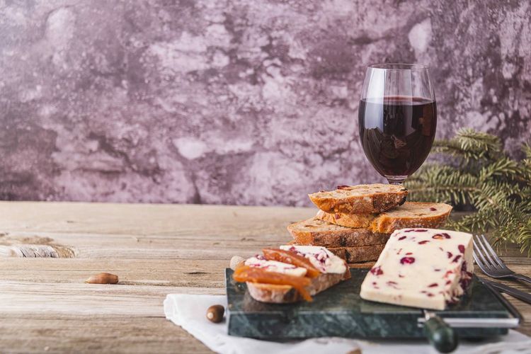Wensleydale cheese with cranberries, red wine, honey, nuts, raisins on wooden cutting board. 
