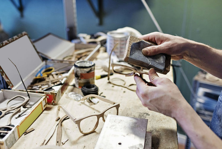 Cropped image of male owner rubbing eyeglasses with work tool at workshop