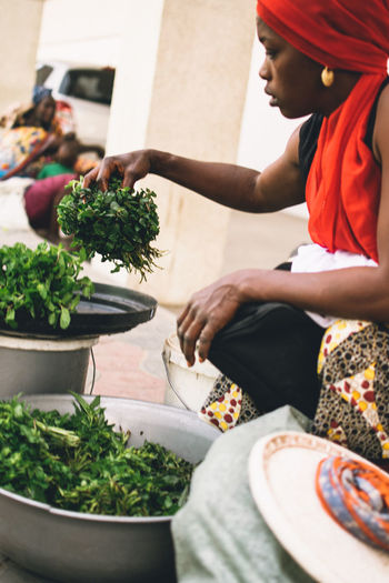 Young woman wearing headscarf holding vegetables while crouching outdoors
