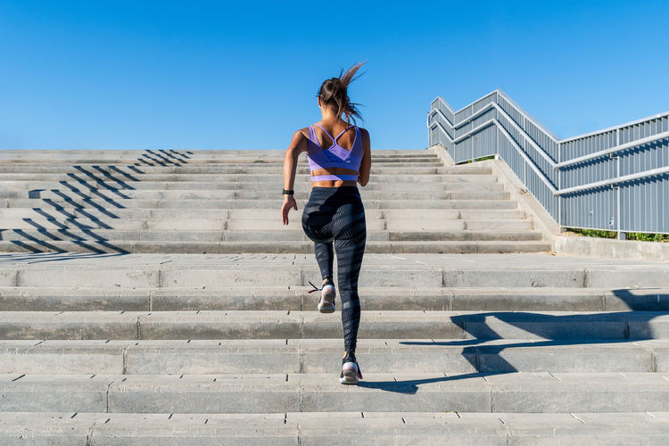 Low angle back view of unrecognizable fit female in activewear running up stone staircase in city during dynamic cardio training