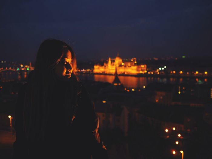 Woman standing by illuminated cityscape against sky at night