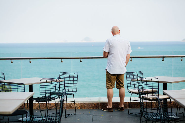 Rear view of man standing on terrace restaurant by sea