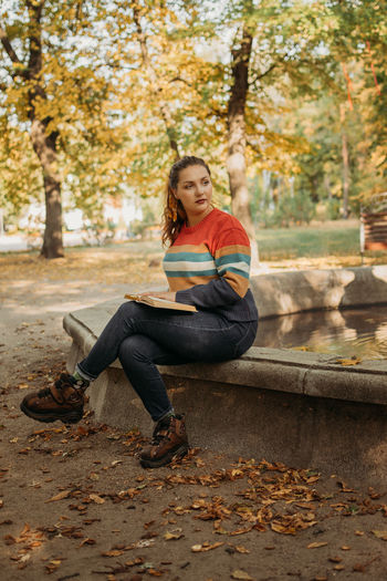 Young plus size woman reading book in fall autumn park in sun lights. body positive, diversity, body 