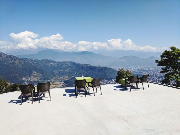 Chairs and tables sitting on chair by mountains against sky