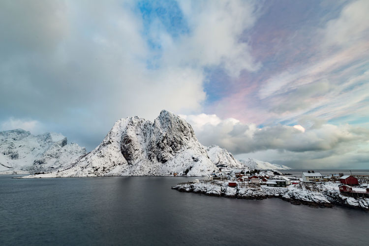 Scenic view of snowcapped mountains by sea against cloud sky
