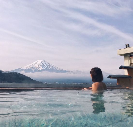 Rear view of shirtless woman in hot spring against snowcapped mt fuji