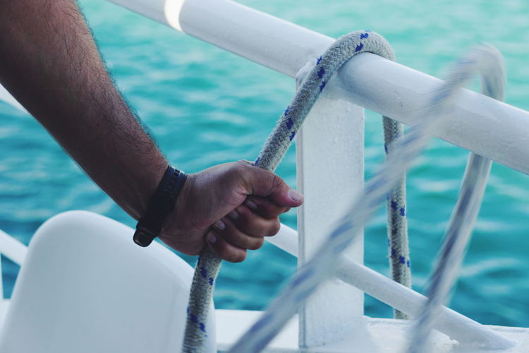 Cropped hand of man holding rope at sea