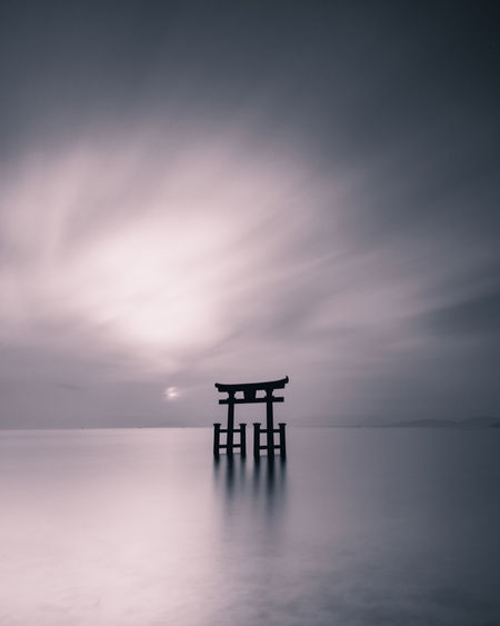 Silhouette lifeguard hut in sea against sky at sunset