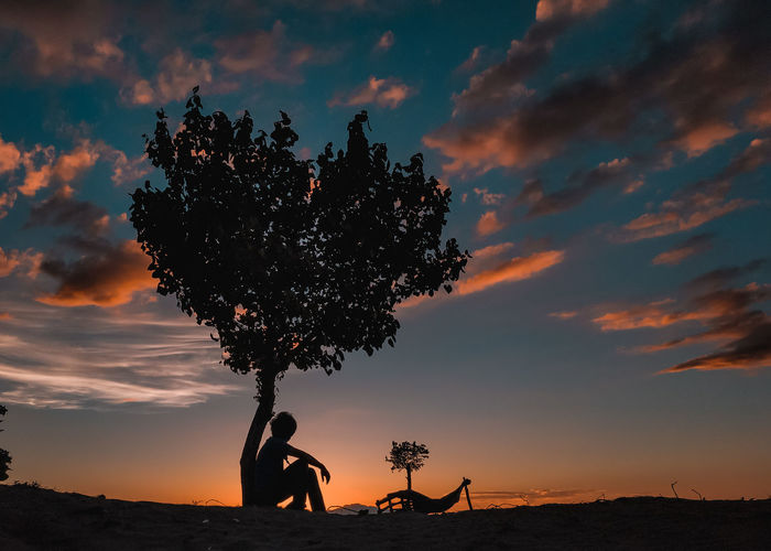 Silhouette man sitting by tree against sky during sunset