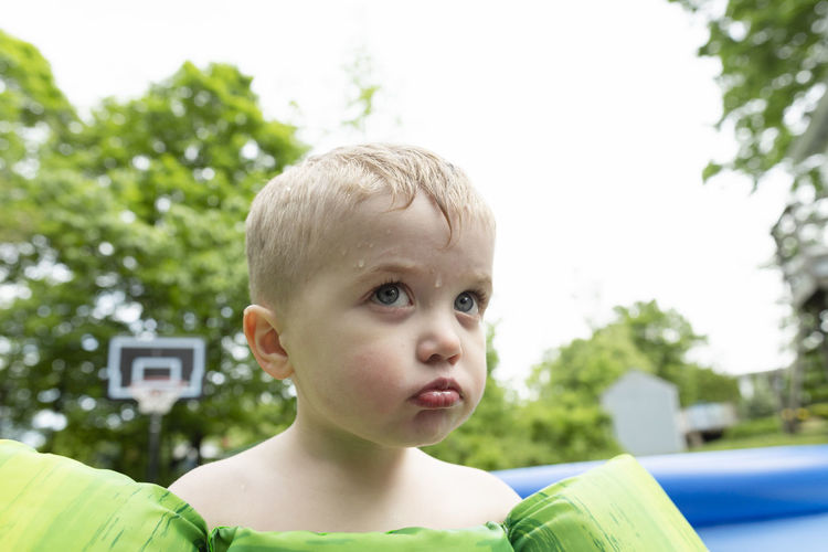 Angry child pouts next to swimming pool while water drips down face
