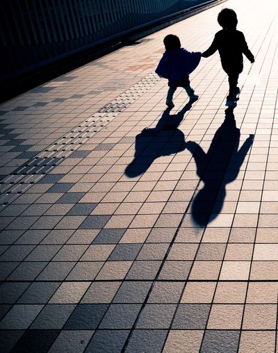 Silhouette siblings walking on footpath in city