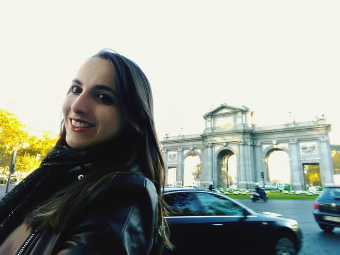 Portrait of smiling young woman in city against clear sky