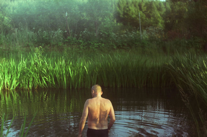 Rear view of shirtless man standing by lake