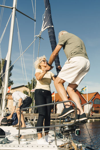Woman helping senior man while boarding boat against sky
