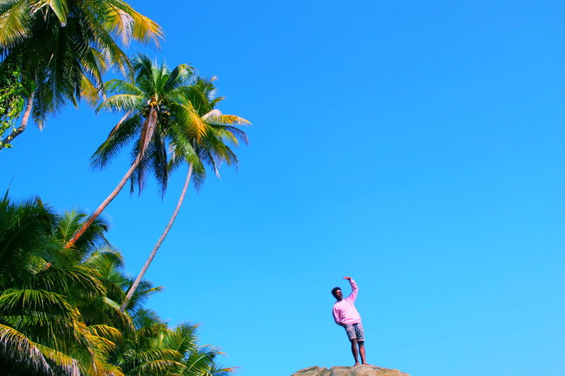 Low angle view of woman standing by palm tree against clear blue sky
