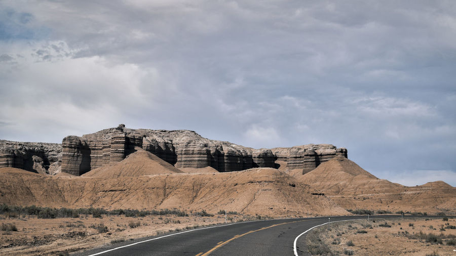Road leading towards rock formations against sky