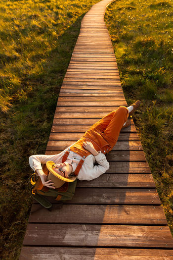 Woman naturalist resting lying on backpack on wooden path through peat bog swamp in national park