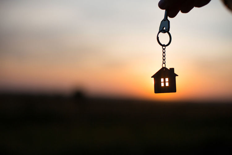 Silhouette of a house figure with a key, a pen with a keychain on the background of the sunset. 