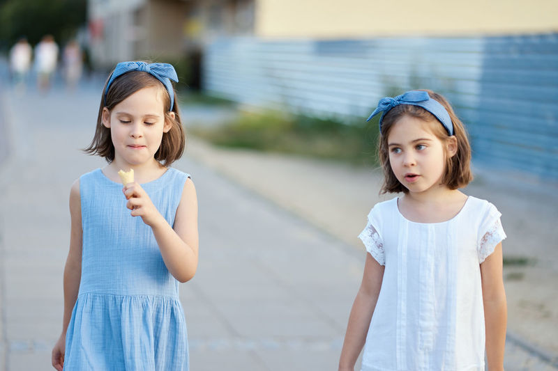 Girl eating ice cream while standing with friend on footpath