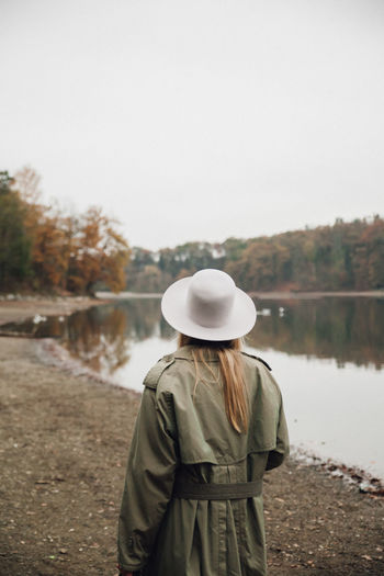 Rear view of woman wearing hat standing by lake against sky