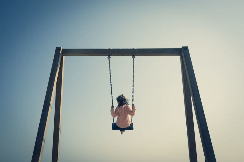 Rear view of girl swinging on swing at playground against clear sky