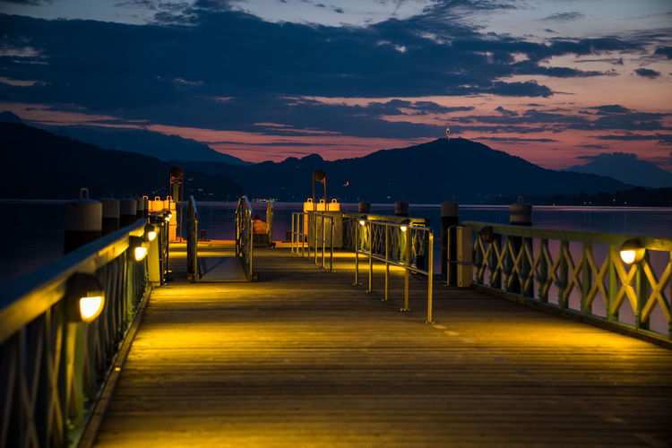 Empty illuminated bridge against sky at sunset