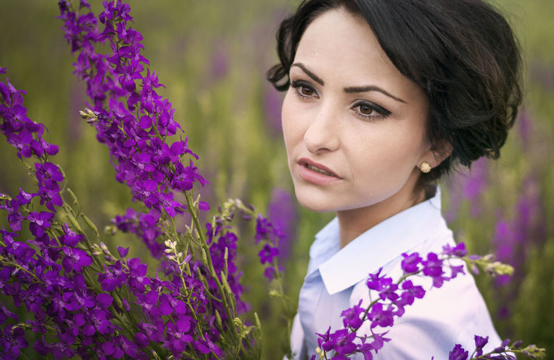 Close-up of young woman by purple flowers on field