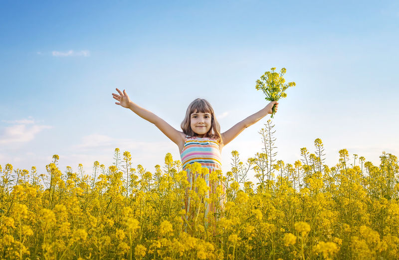 Young woman standing amidst yellow flowering plants on field against sky