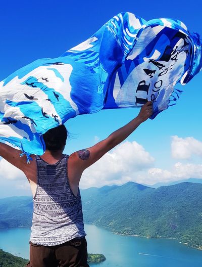 Rear view of man holding scarf while standing against sky