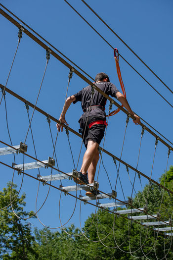 Low angle view of man climbing on cable against sky