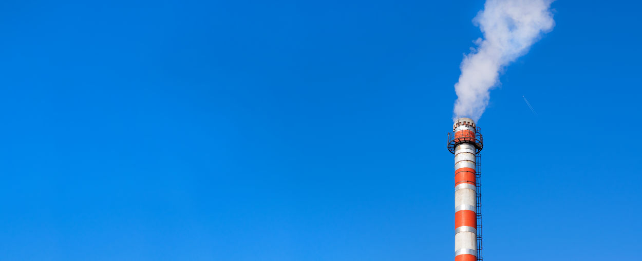 Factory chimney against the clear blue sky. plane flying in the background. wide banner