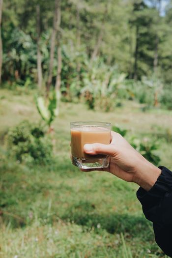 Midsection of person holding drink against plants