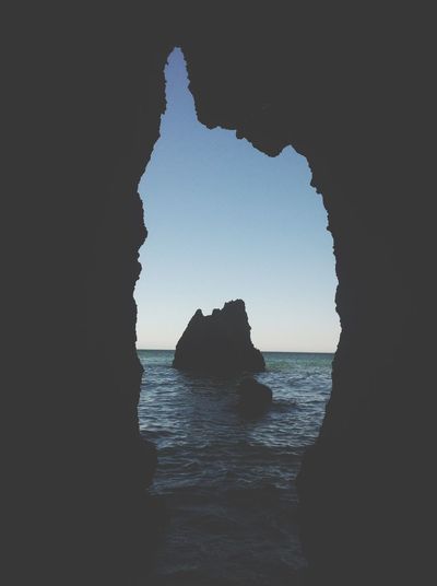 Silhouette rock formation in sea against sky