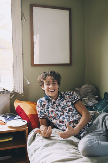 Portrait of cheerful teenage boy leaning on bed at home
