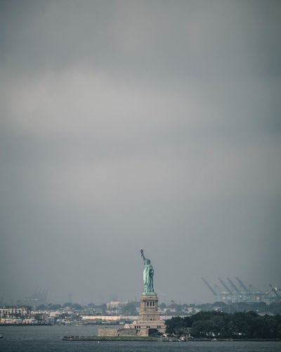 Statue of liberty by river against cloudy sky